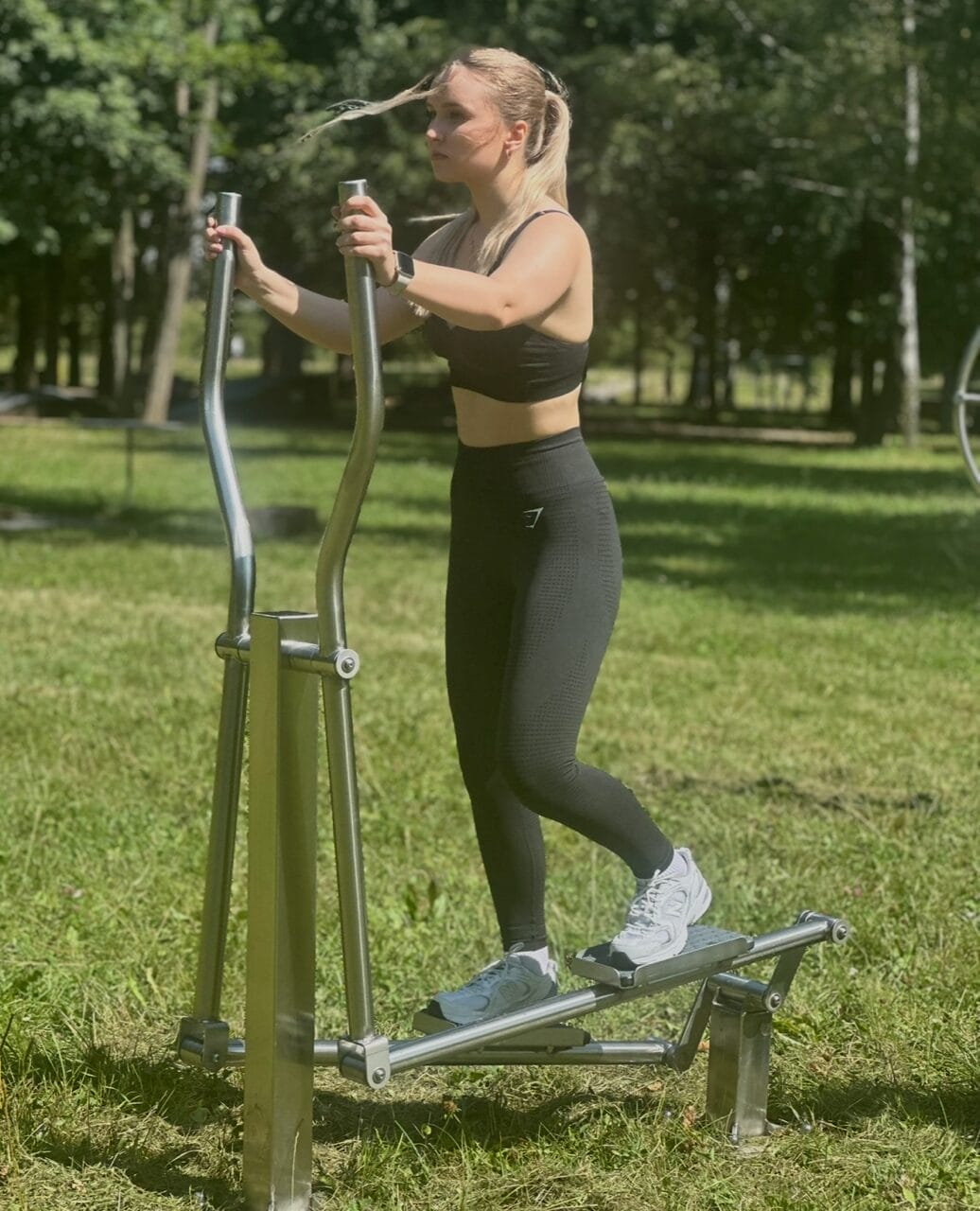 mladá žena cvičí v parku na stroji orbitrek